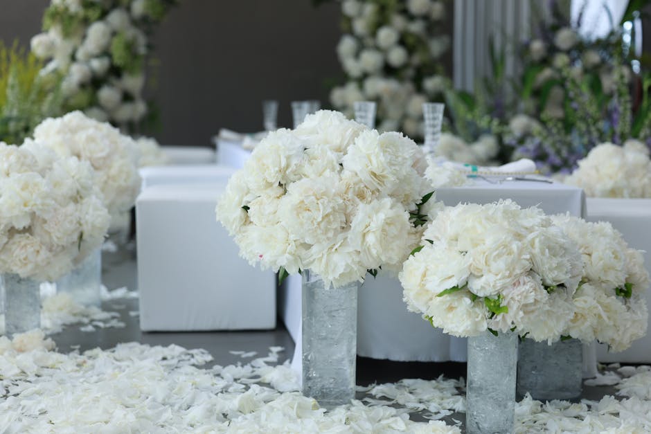 A floral arrangement featuring large, lush white hydrangeas and roses, forming bouquet-like clusters placed in modern, rectangular concrete vases. The flowers are fresh, with soft, textured petals and