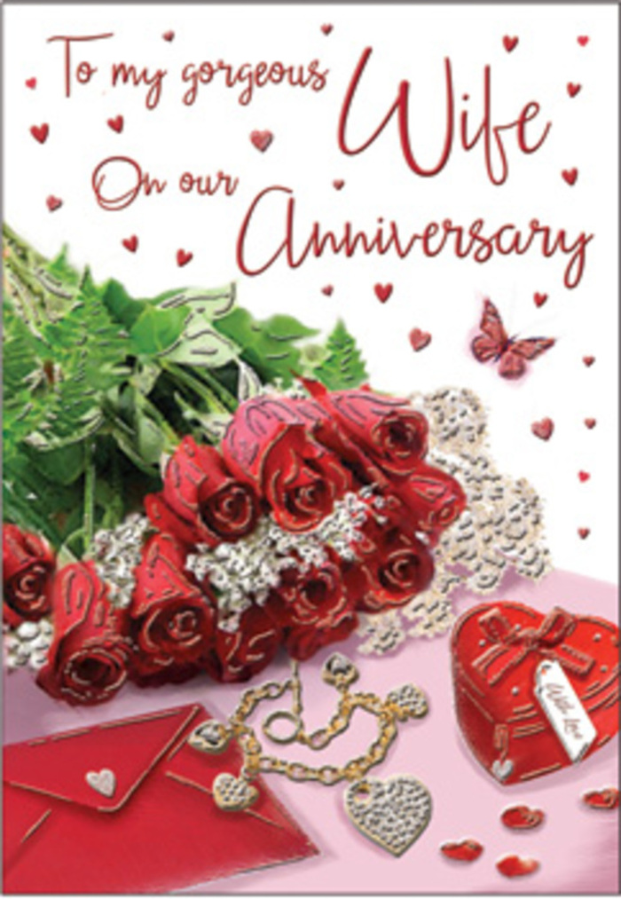 A richly composed anniversary scene unfolds as if laid out on a dressing table before a special night in Biggin Hill. At the centre, a modest yet luxuriant bouquet of classic red roses is nestled close to a standing greeting card, the blooms so full and velvety they almost seem to breathe. Each rose curls outward in layered spirals of deep crimson, while fresh green foliage peeks between the blossoms, adding gentle contrast and depth. The card itself stands open just enough to suggest a heartfelt message inside, and beside it lies a neatly placed envelope, ready to be kept as a cherished memento. A small piece of jewellery, perhaps a necklace or charm, rests near a heart-shaped box, their metallic and satin finishes catching the ambient light, hinting at treasured gifts exchanged over the years. Scattered around are delicate heart accents and tiny sparkling elements, like confetti from an intimate celebration at home. A solitary butterfly motif introduces a touch of whimsy and hope, symbolising a love that has grown and transformed over time. The lighting is gentle and diffused, casting soft shadows that emphasise the roses' curves and the subtle textures of card, ribbon, and polished metal. The whole arrangement feels deliberately unhurried, the way a local couple might prepare a table in their Biggin Hill living room before opening a bottle of wine. It conveys a quiet, enduring romance, where the fragrance of fresh roses and the rustle of an anniversary card say what words sometimes cannot.